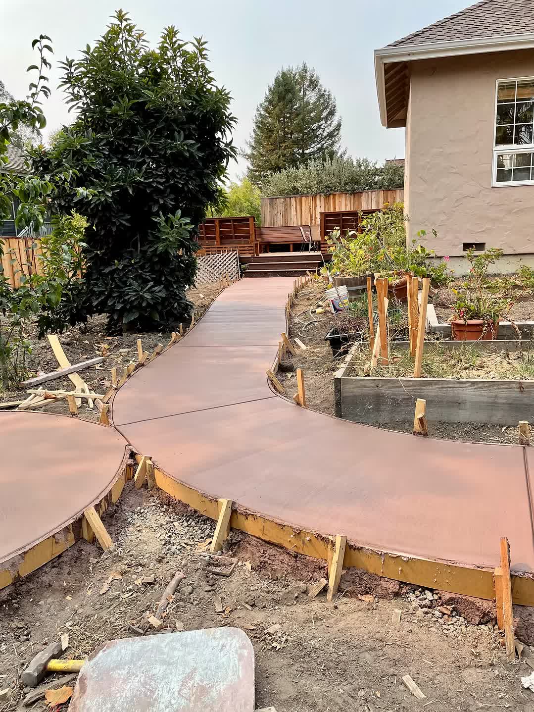 Freshly poured curved concrete walkway through a Santa Cruz backyard, framed by wood stakes and forms